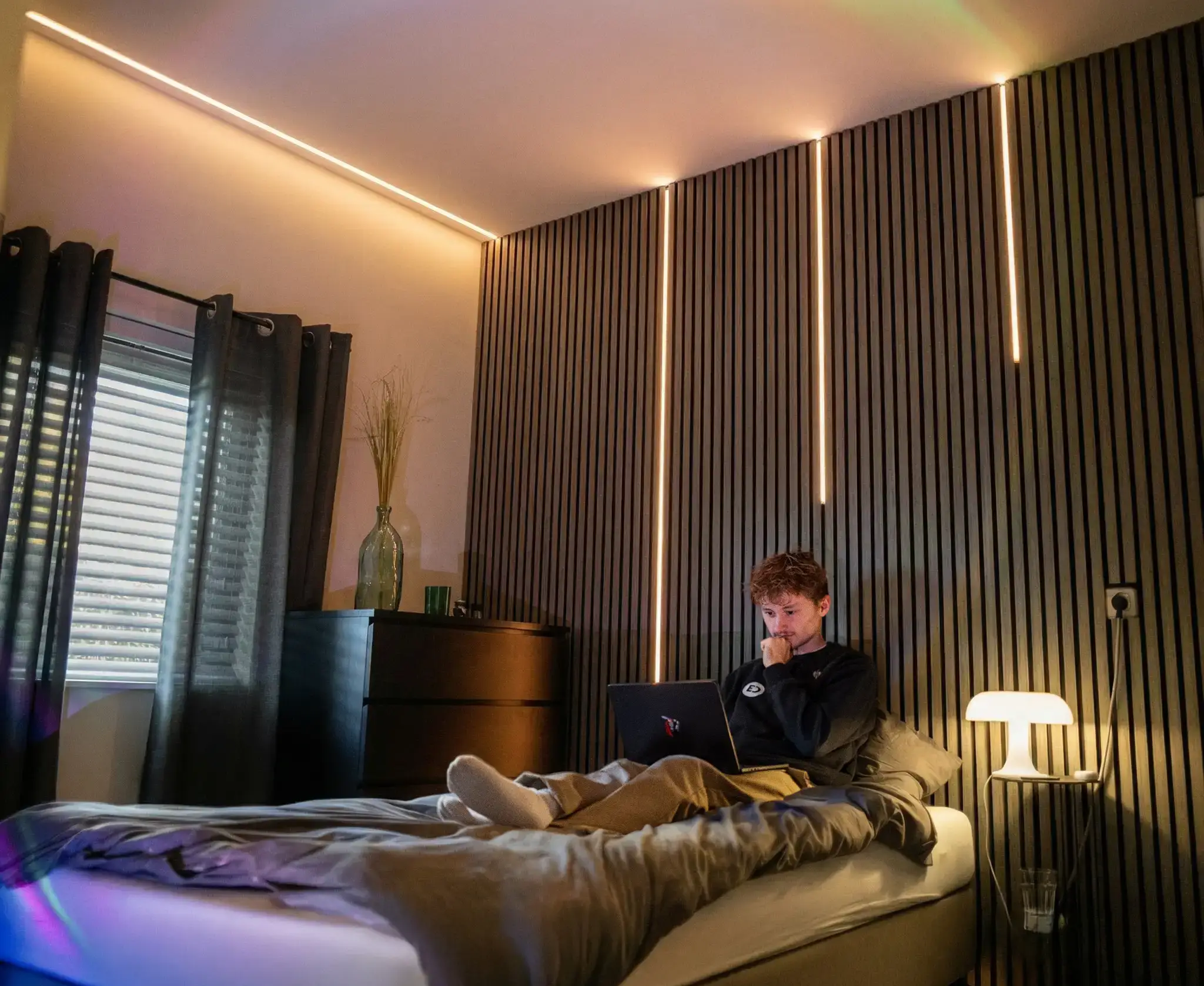 Slaapkamer met warme LED-strips langs plafond en verticale wandlatten voor sfeervolle verlichting.